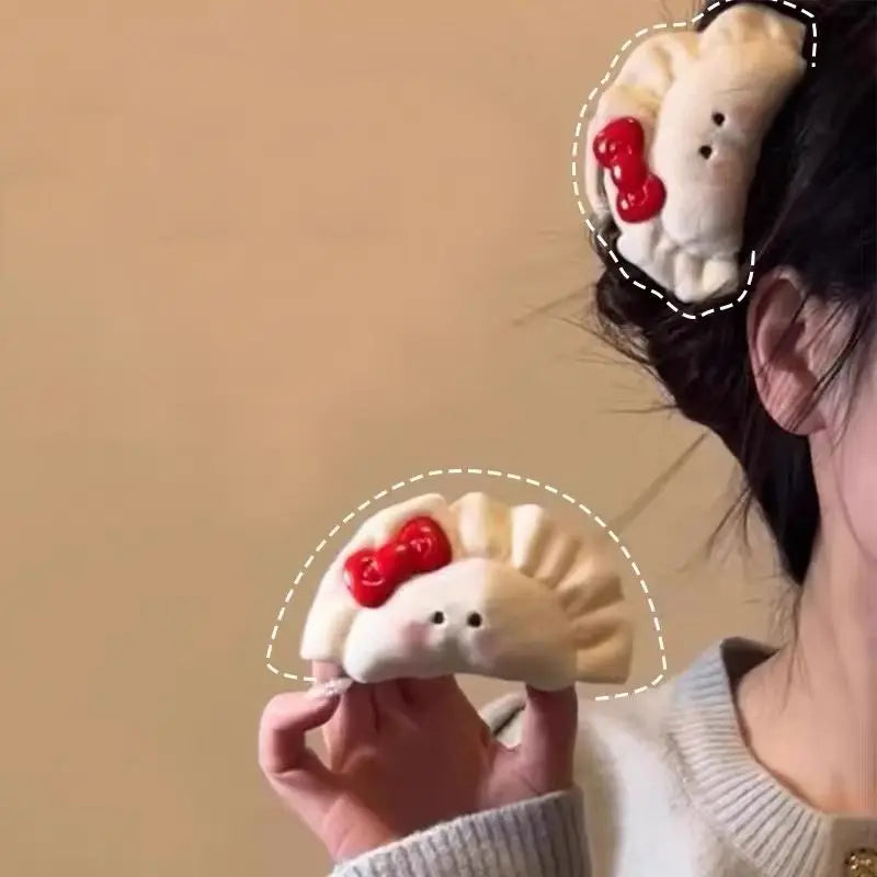 A person holds and wears a cute dumpling-shaped hair clip with a red bow. The clip is shown in two views: one held in the hand and one styled in a hair accessory, against a plain beige background.