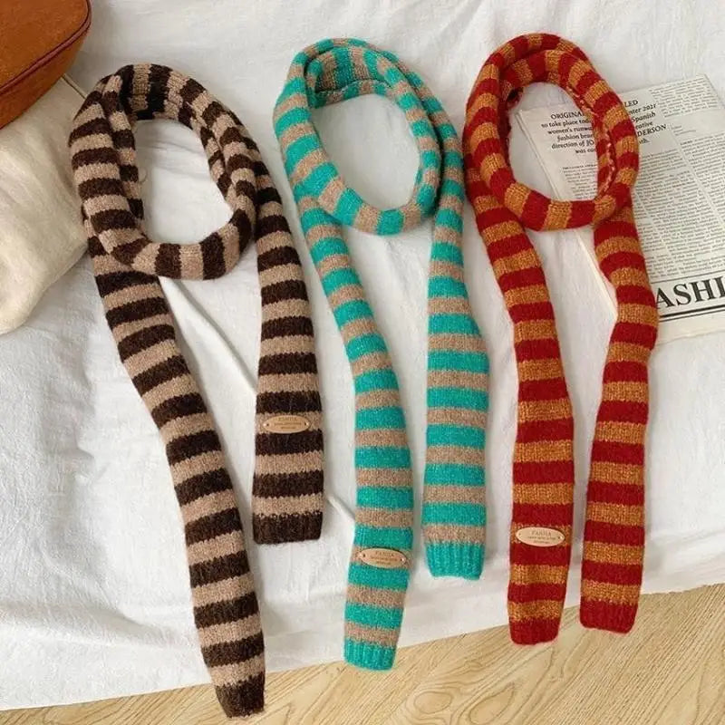 Three striped scarves in brown, green, and red on a white surface with a newspaper.