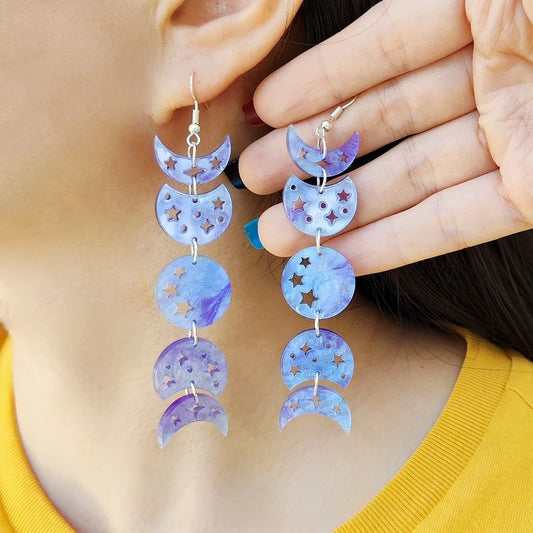 Person wearing purple moon-shaped earrings with star details.