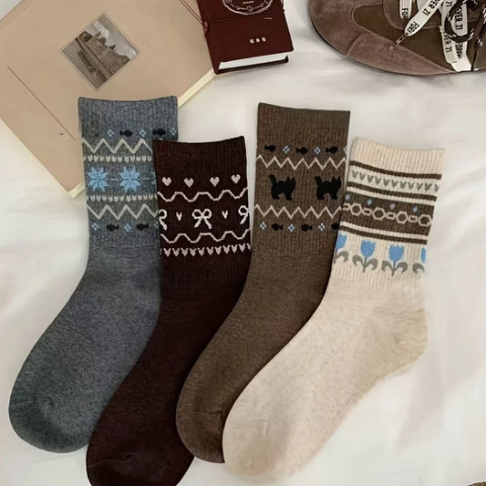 Four pairs of patterned crew socks laid flat on a white surface: one heather gray with blue and white Nordic motifs, one dark brown with white heart and bow patterns, one taupe-brown with black dog silhouettes, and one cream with blue and brown floral/Fair Isle patterns.