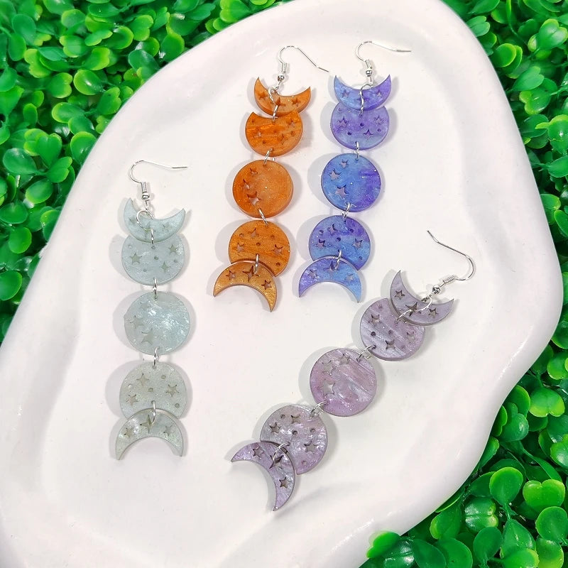Colorful moon-shaped earrings on a white dish with green leaves in the background