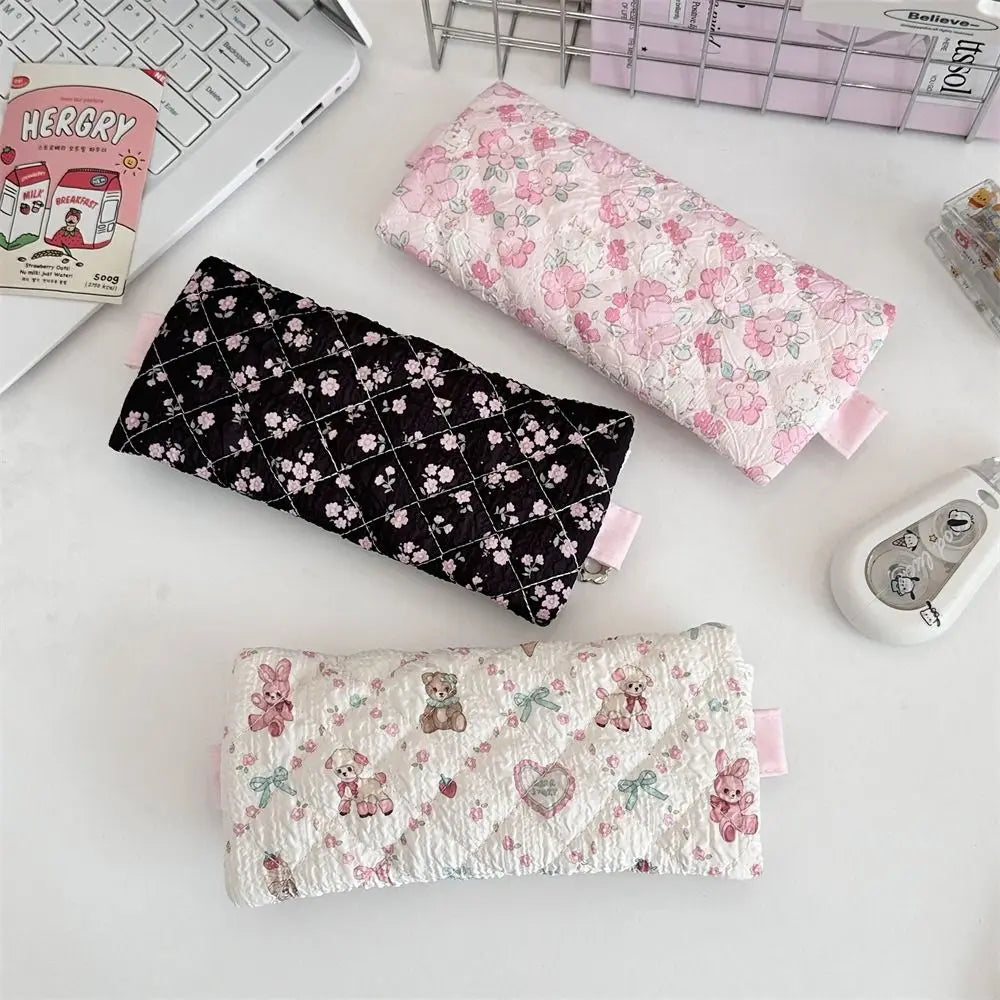 Three floral-patterned pouches on a desk with a keyboard and stationery items.