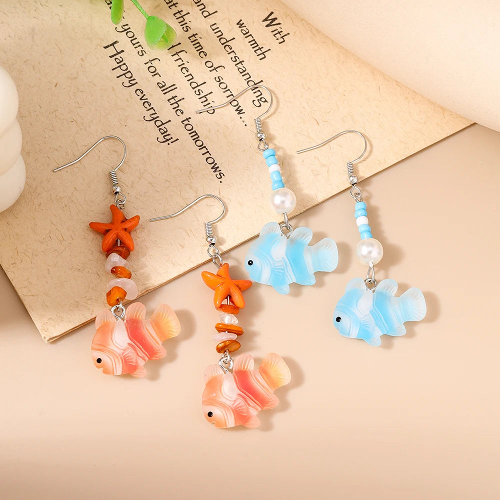 Pair of earrings with fish and starfish designs on a textured surface