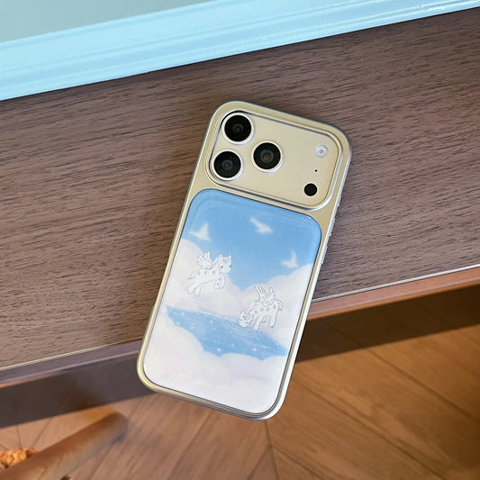 A gold-colored phone case with a printed sky and cloud design, shown resting on a wooden table.