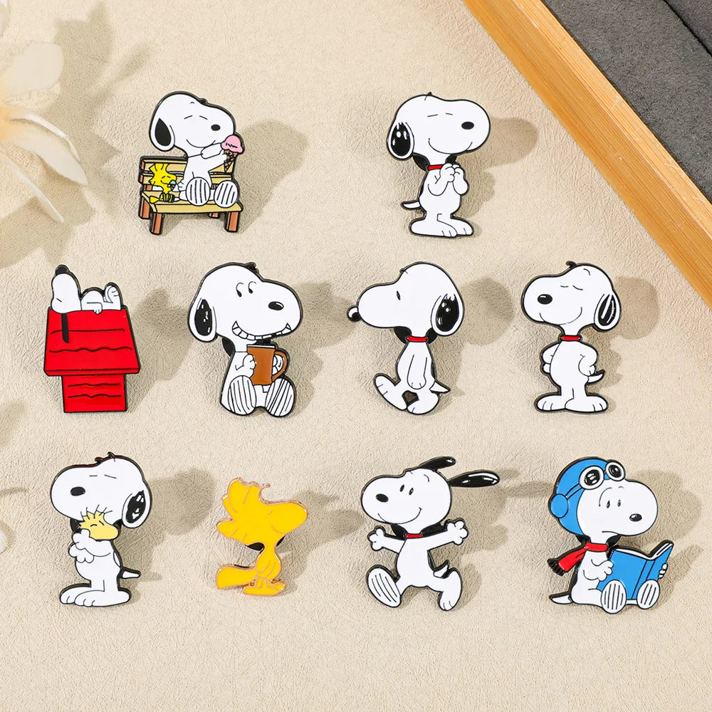 Ten enamel pins featuring different cartoon designs of Snoopy and Woodstock on a beige textured background.