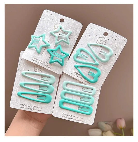Four pastel hair clips in mint green and light blue-green are displayed on white card backing, with a hand holding the set against a soft beige background.