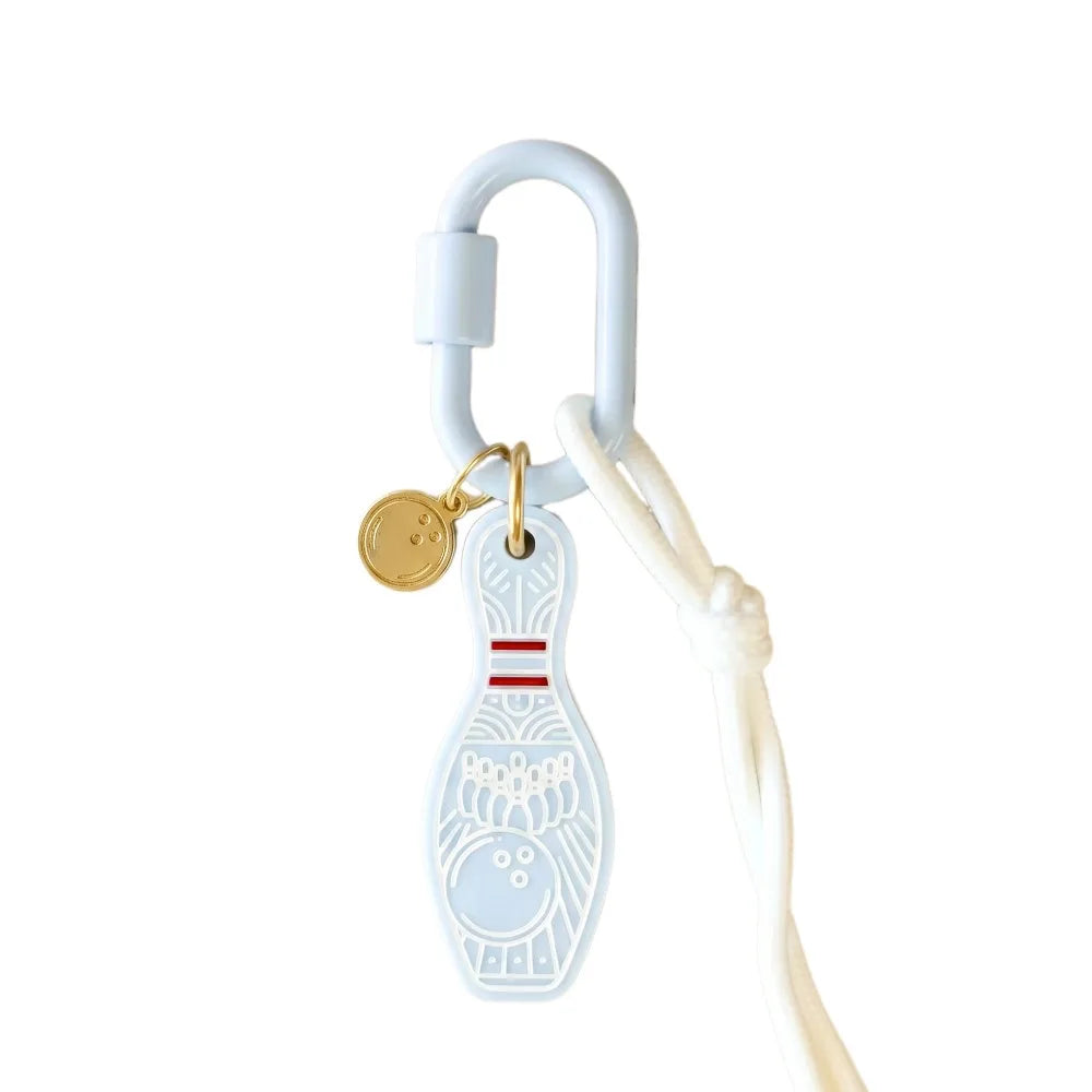 A white silicone bowling pin keychain charm with a gold coin tag and a white carabiner, shown on a plain white background.