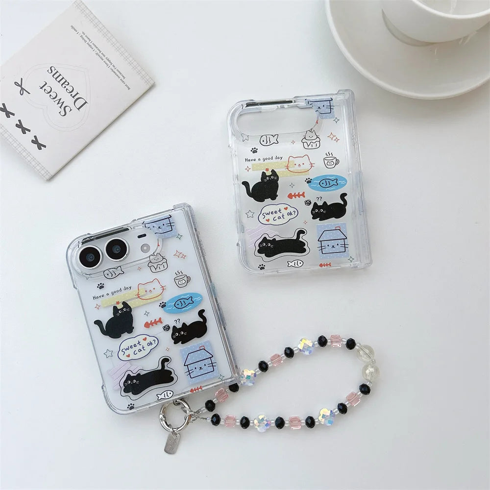 Two clear iphone duo cases with cute cartoon cat illustrations and a beaded wrist strap, arranged on a white surface with a small card and cup in the background.
