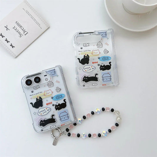Two clear iphone duo cases with cute cartoon cat illustrations and a beaded wrist strap, arranged on a white surface with a small card and cup in the background.