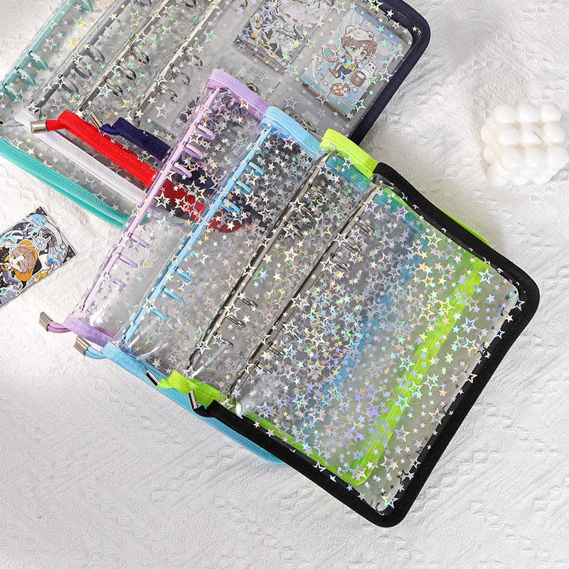A set of clear plastic binder rings decorated with iridescent star-shaped stickers, shown open on a white textured fabric background. The rings feature colorful trim in teal, purple, light blue, and lime green, and contain various stationery items.