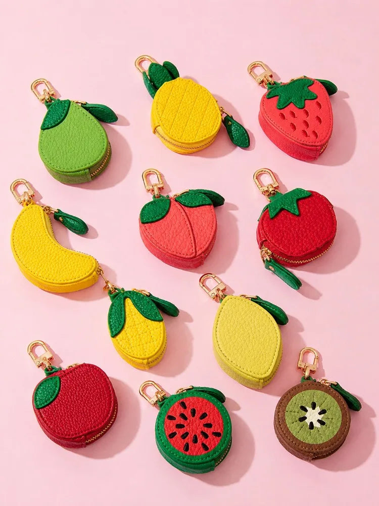 A collection of small, fruit-shaped zippered coin pouches in various colors, including green avocado, yellow banana and lemon, red strawberry, peach, watermelon, and kiwi, arranged on a solid pink background.