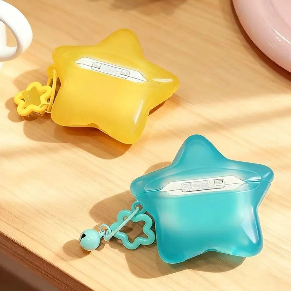 Two translucent star-shaped protective cases for wireless earbuds, one in yellow and one in light blue, each with a small flower charm and bell, displayed on a light wood surface.