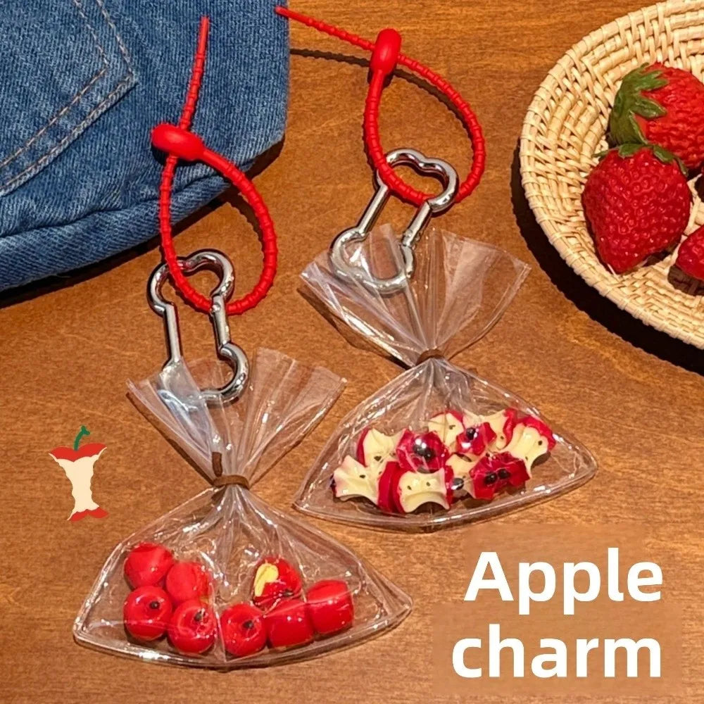Apple-shaped charm with red string on a wooden surface, next to denim fabric and a woven basket with strawberries.