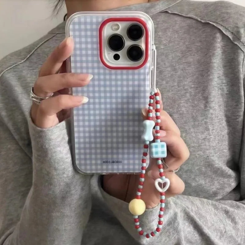 Person holding a phone with a checkered case and decorative strap