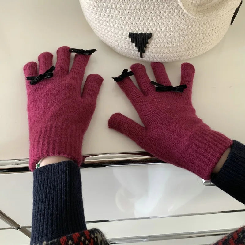 Purple gloves with black bows worn on a white surface with a hat in the background