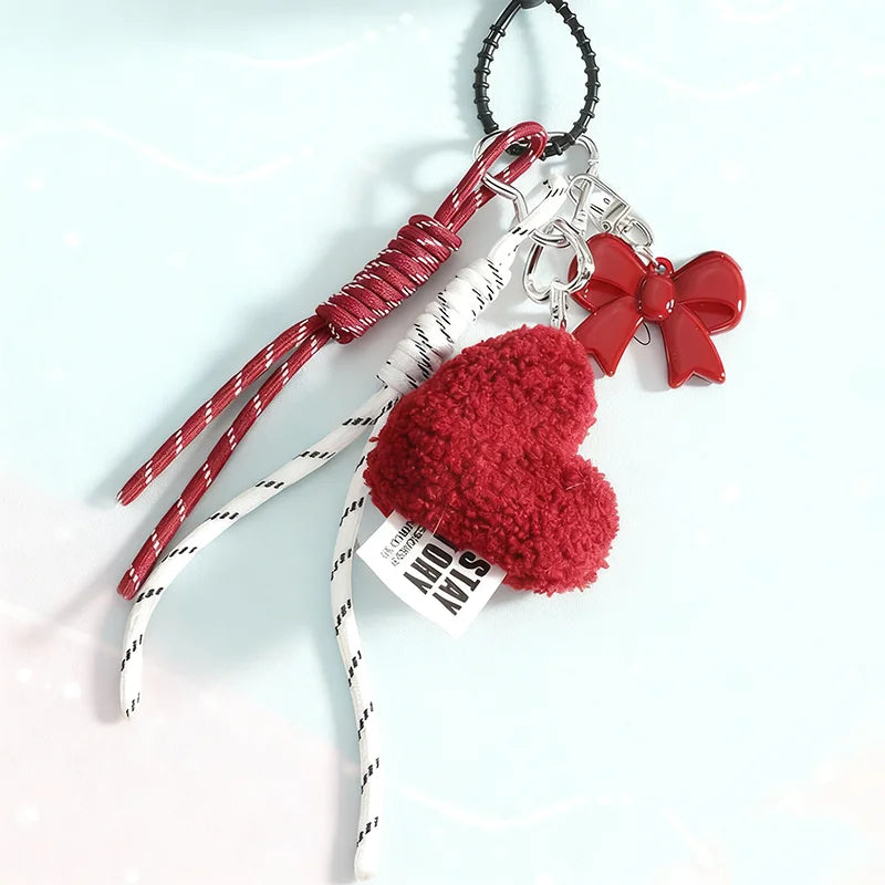 A red and white Valentine's Day themed keychain featuring a fuzzy red heart, a red bow charm, a red wrapped cord, and white rope with black stripes, attached to a black key ring.