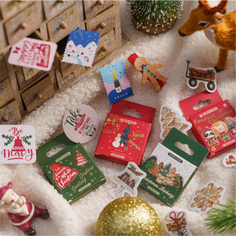 A styled flat-lay of Christmas-themed sticker products arranged on white faux fur with holiday props, including a wooden advent calendar, ornaments, a reindeer figurine, and festive cards and sticker packs.