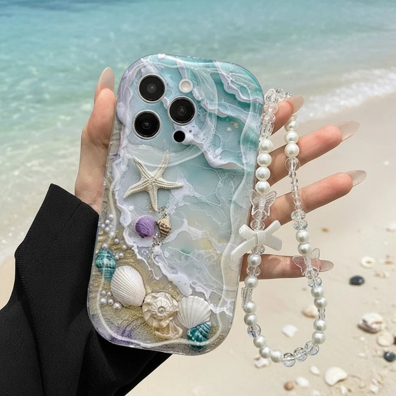 Phone case with seashell and starfish design held by a hand on a beach.