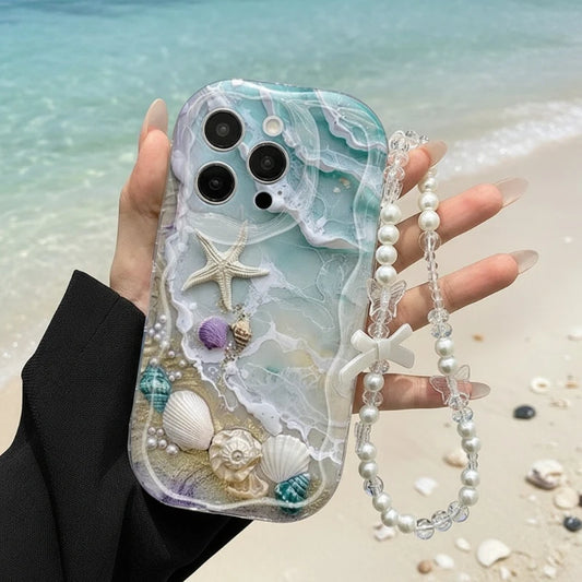 Phone case with seashell and starfish design held by a hand on a beach.