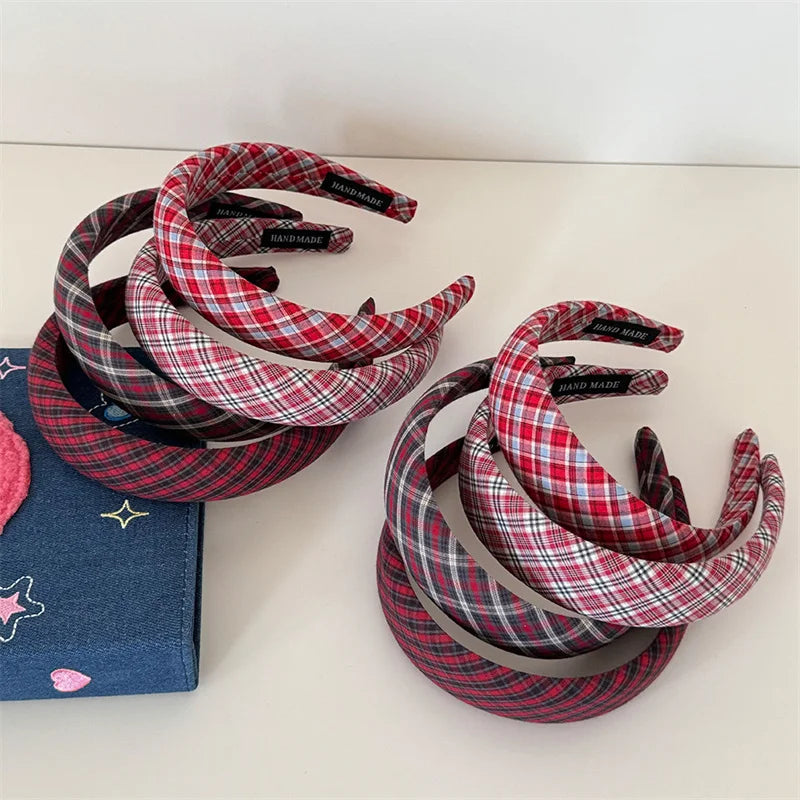 Two coiled stacks of plaid fabric headbands on a light beige surface, with one stack resting on a blue star-patterned fabric box. The headbands feature red, pink, gray, and white tartan plaid patterns.