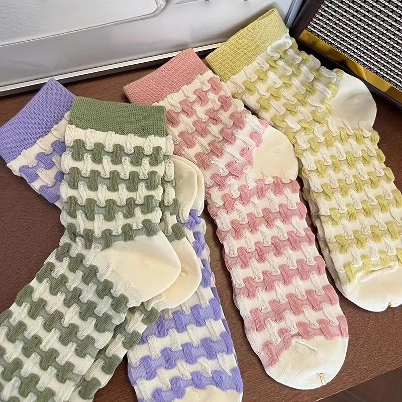Four pairs of textured waffle-knit ankle socks arranged on a wooden surface, featuring pastel green, lavender, pink, and pale yellow colorways with a waffle pattern.