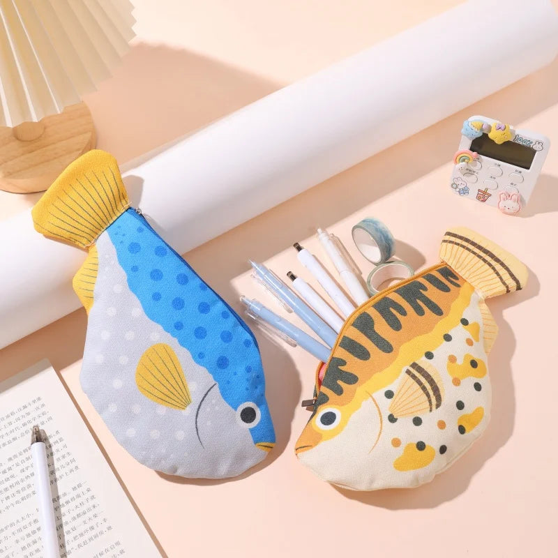 Two fish-shaped pencil cases on a light pink surface with stationery items.