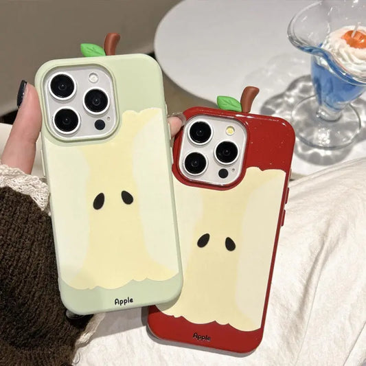 Two Apple iPhone cases featuring a cute ghost-like apple design, held in a hand. One case is a pale sage green with a cream-colored apple slice graphic, and the other is red with a matching cream graphic.