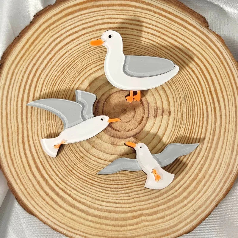 Three seagull brooches on a wooden surface