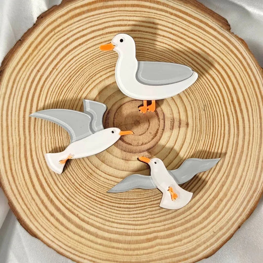 Three seagull brooches on a wooden surface