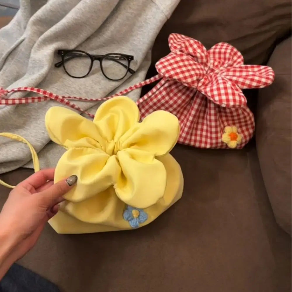 Yellow flower-shaped bag held by a hand with a red and white checkered bag in the background.