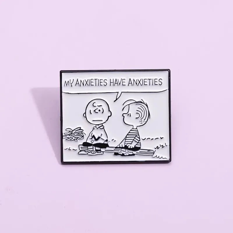 A rectangular enamel pin featuring a black and white cartoon illustration of two characters sitting by a campfire, with a speech bubble reading 'MY ANXIETIES HAVE ANXIETIES'. The pin is centered on a solid light lavender background.
