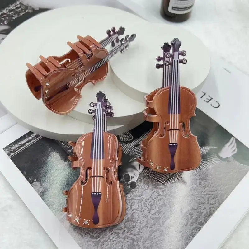 Three miniature brown violin-shaped hair clips arranged on white circular platforms and a printed magazine page, with a dark bottle partially visible in the background.