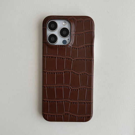A dark brown crocodile-embossed leather phone case on a silver iPhone, shown from the back against a light gray background.