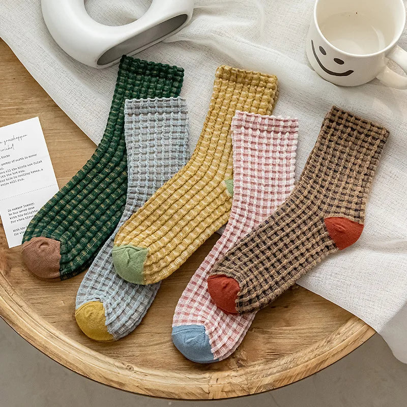 Set of colorful checkered socks on a wooden tray with a white mug and paper in the background.