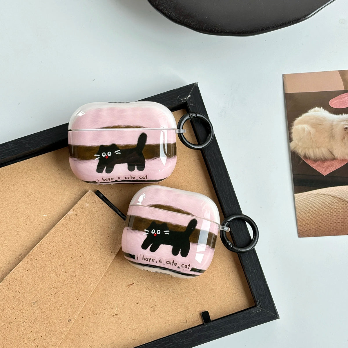 Pink airpod cases with black cat designs on a light surface.