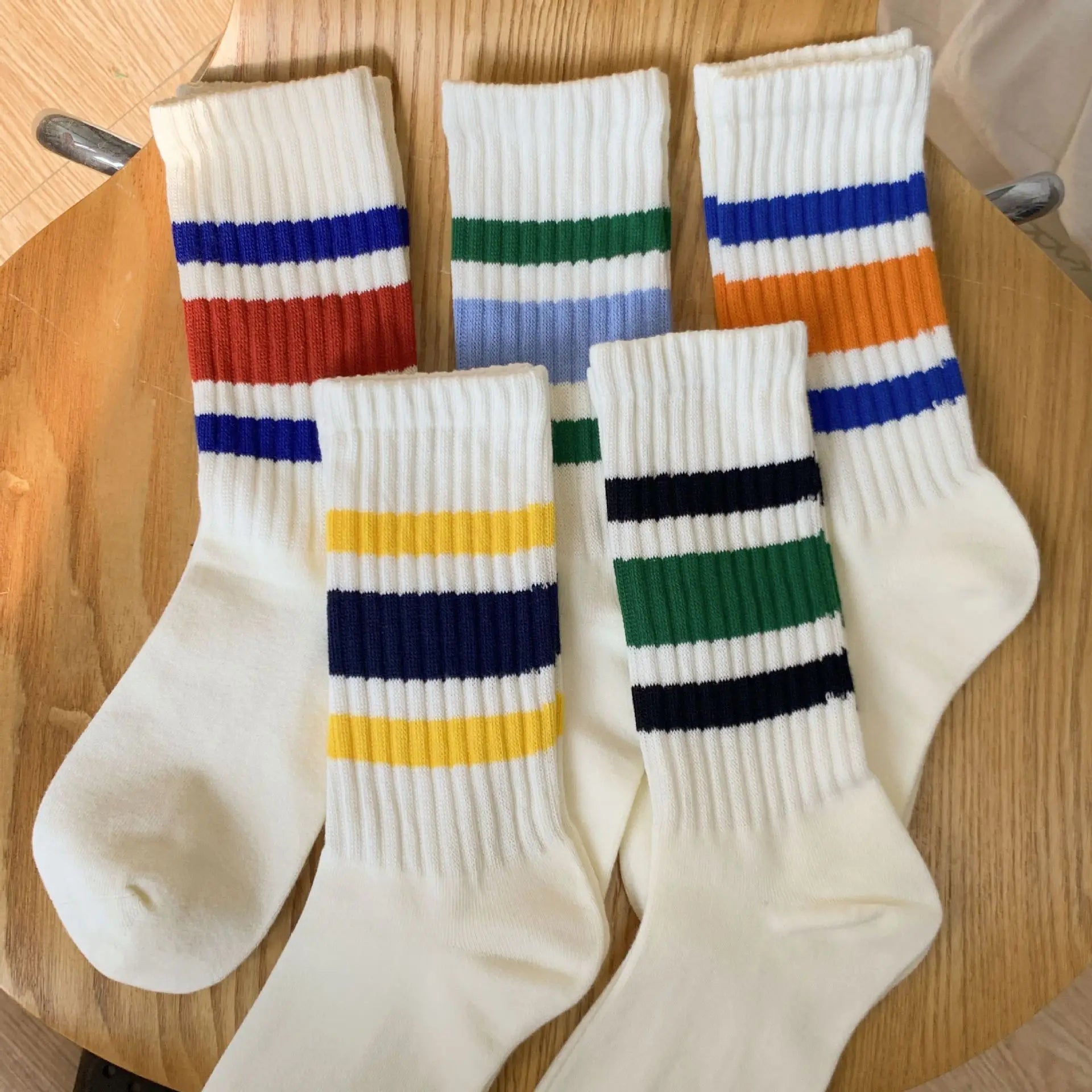 Five pairs of white ribbed crew socks with colorful horizontal stripes, arranged on a round wooden table.