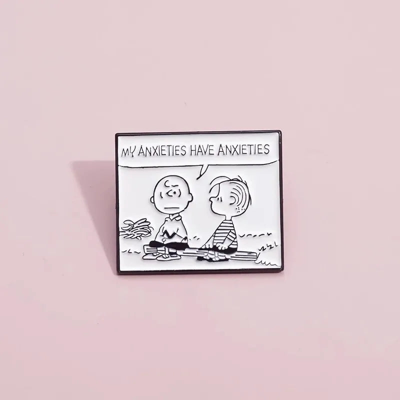 A square enamel pin featuring a black and white cartoon illustration of two characters sitting on a log, with a speech bubble reading 'MY ANXIETIES HAVE ANXIETIES', displayed on a solid light pink background.