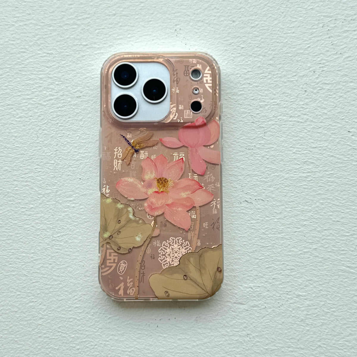 A clear phone case featuring a pink lotus flower, green lotus leaves, and traditional Chinese calligraphy characters on a light beige background, shown on a white textured wall.