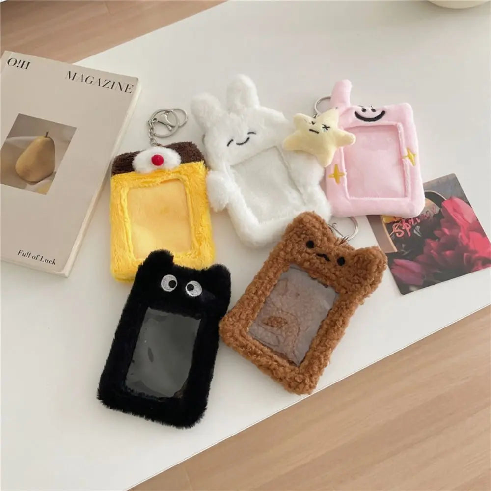 Five plush photocard pouches with keychains in different colors and cute character designs, arranged on a white tabletop with a magazine and card nearby.