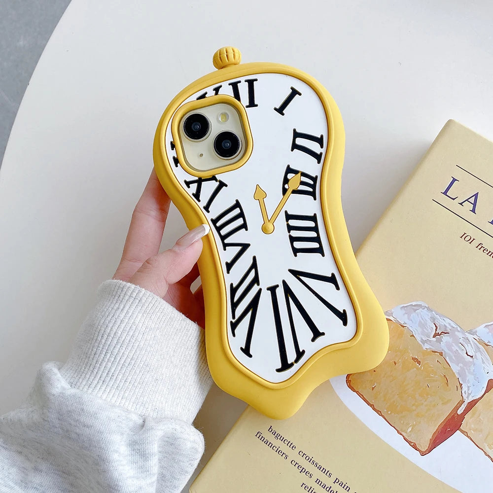 A hand wearing a white knit sleeve holds a yellow phone case designed to look like a melting clock with black Roman numerals and gold hands, set against a light background with a book.