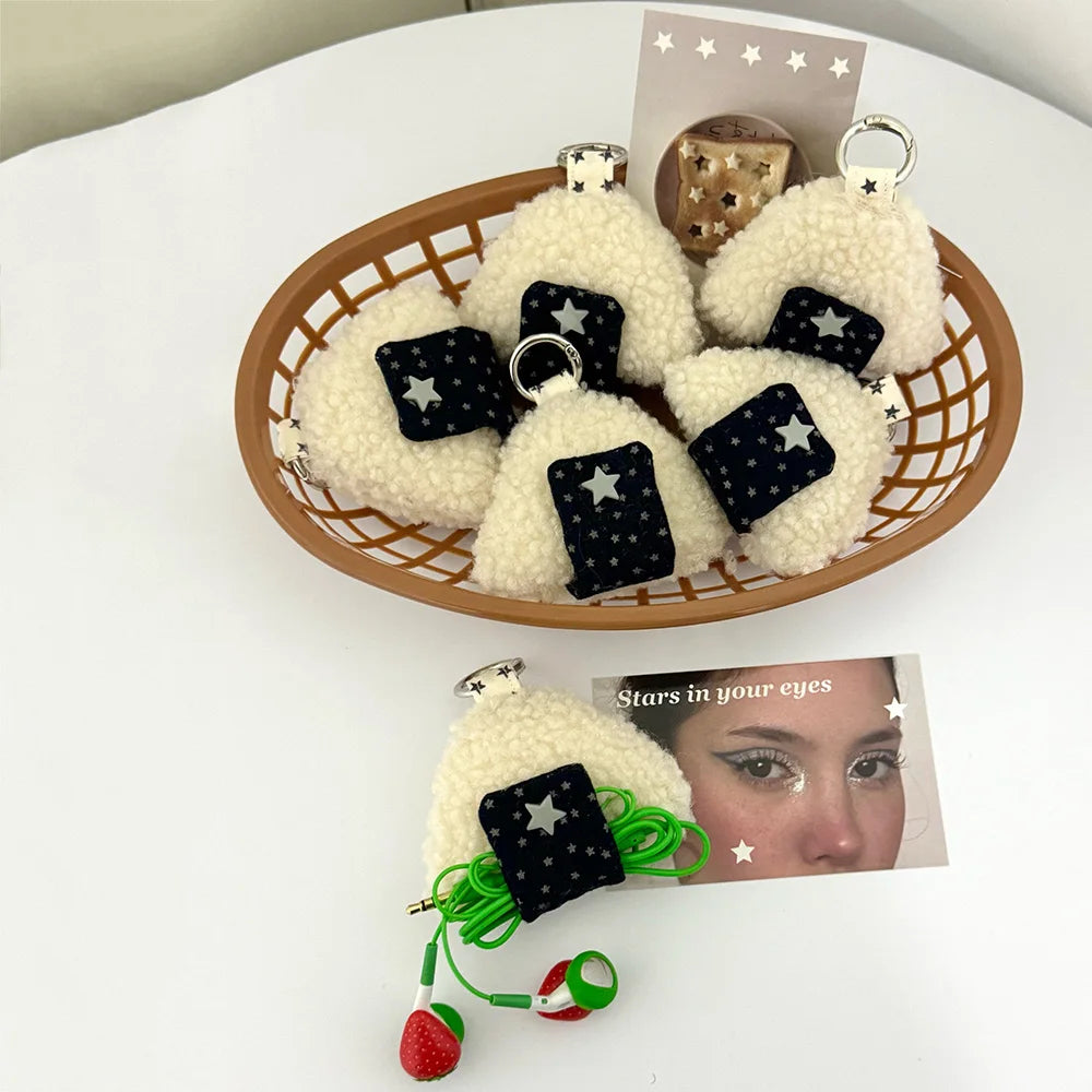 Fuzzy white rice-pan-shaped keychain charms with black star-patterned squares, displayed in a woven basket and on a white surface with a printed card.