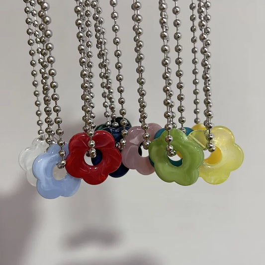 Colorful flower-shaped pendants on metal chains against a neutral background