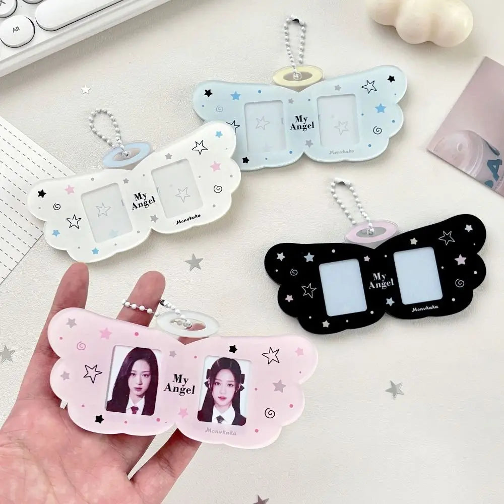 Three butterfly-shaped photo ID keychains in white, light blue, and black are displayed on a light desk surface, with one held in a hand. Each keychain has two photo slots, small star and moon illustrations, and a silver keychain ring.