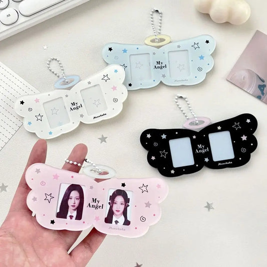 Three butterfly-shaped photo ID keychains in white, light blue, and black are displayed on a light desk surface, with one held in a hand. Each keychain has two photo slots, small star and moon illustrations, and a silver keychain ring.