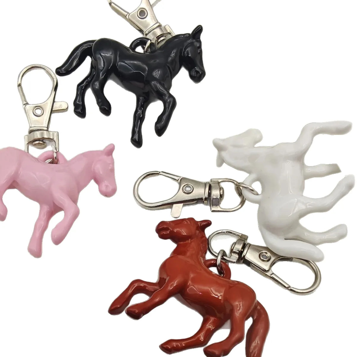 Four small horse-shaped keychain charms in black, pink, white, and reddish brown, each attached to a silver lobster clasp, shown on a plain white background.