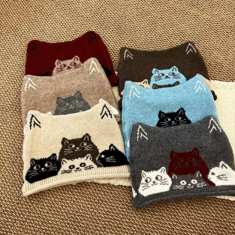 Six pairs of knit cat-themed beanie hats are arranged in two columns on a textured beige carpet. Each pair features multiple cat faces knitted into the design, with different background colors for the hats including burgundy, taupe, cream, dark brown, light blue, and charcoal gray.