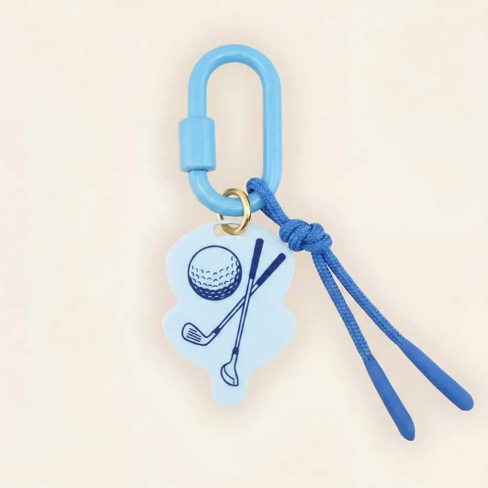 A golf-themed keychain or bag charm with a light blue carabiner, blue cord, and a light blue silhouette charm printed with a golf ball and crossed clubs, shown on a plain beige background.