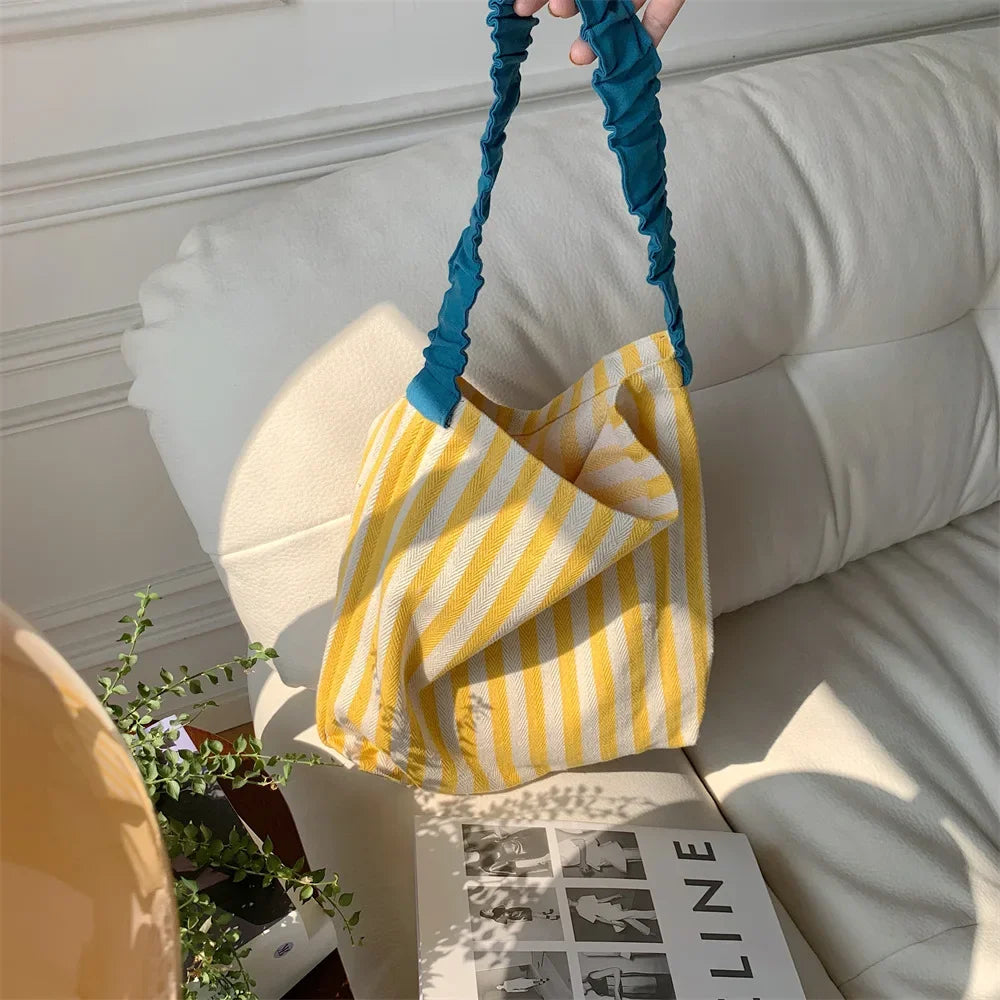 Yellow and white striped bag with blue handle held over a light-colored sofa.