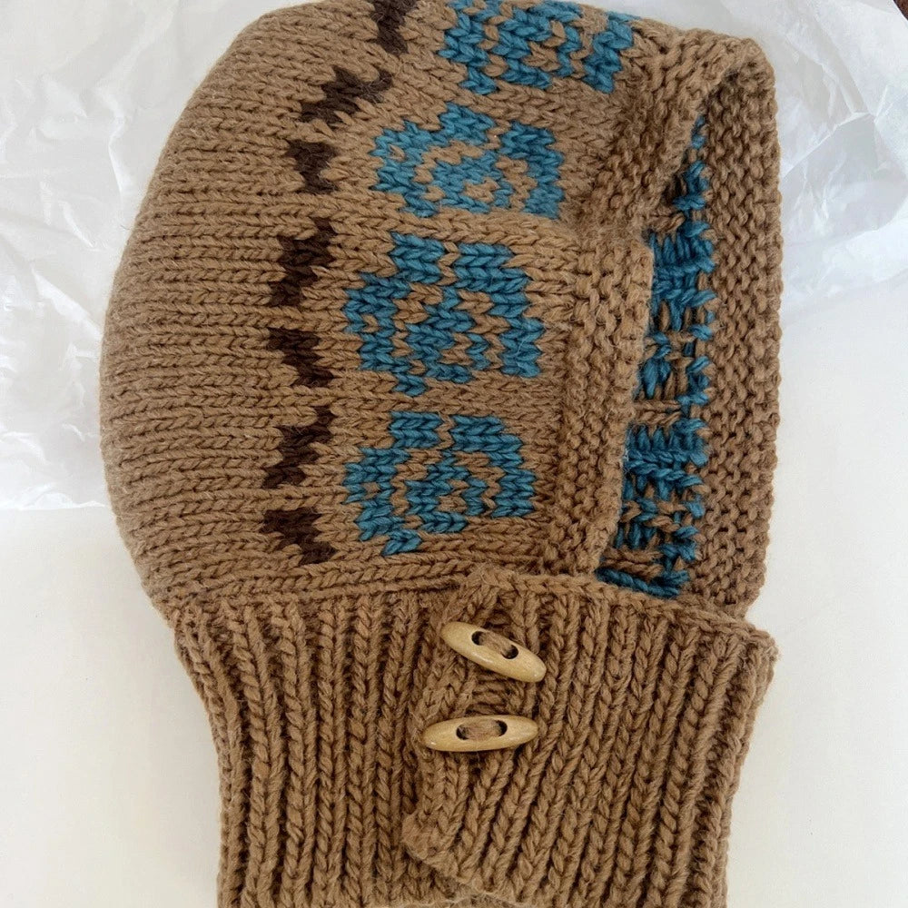 A hand-knitted brown beanie hat featuring blue and dark brown Fair Isle patterns, with a ribbed cuff and two wooden buttons, laid flat on a white background.