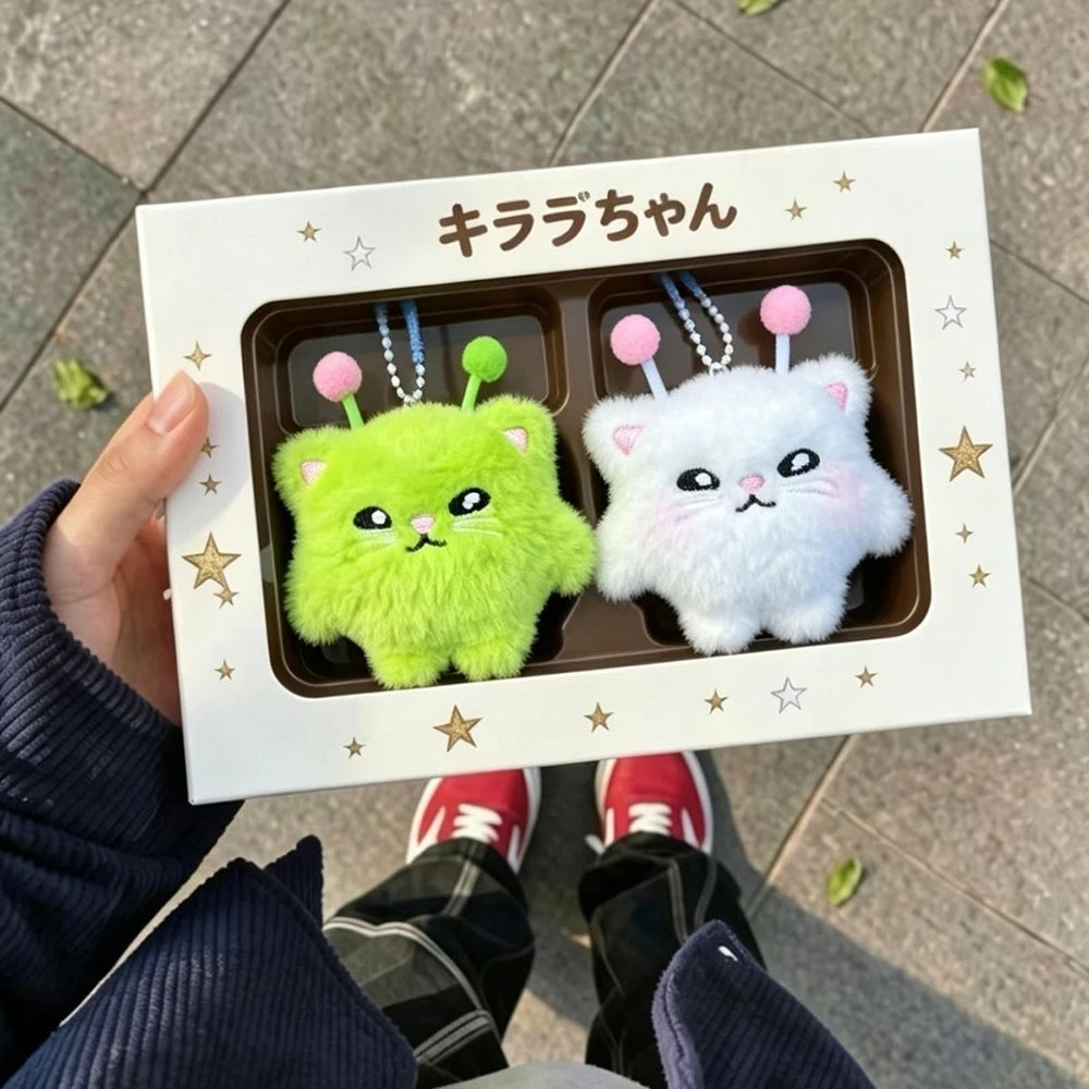 Two small plush toys, one green and one white, in a box with Japanese text on a pavement background.
